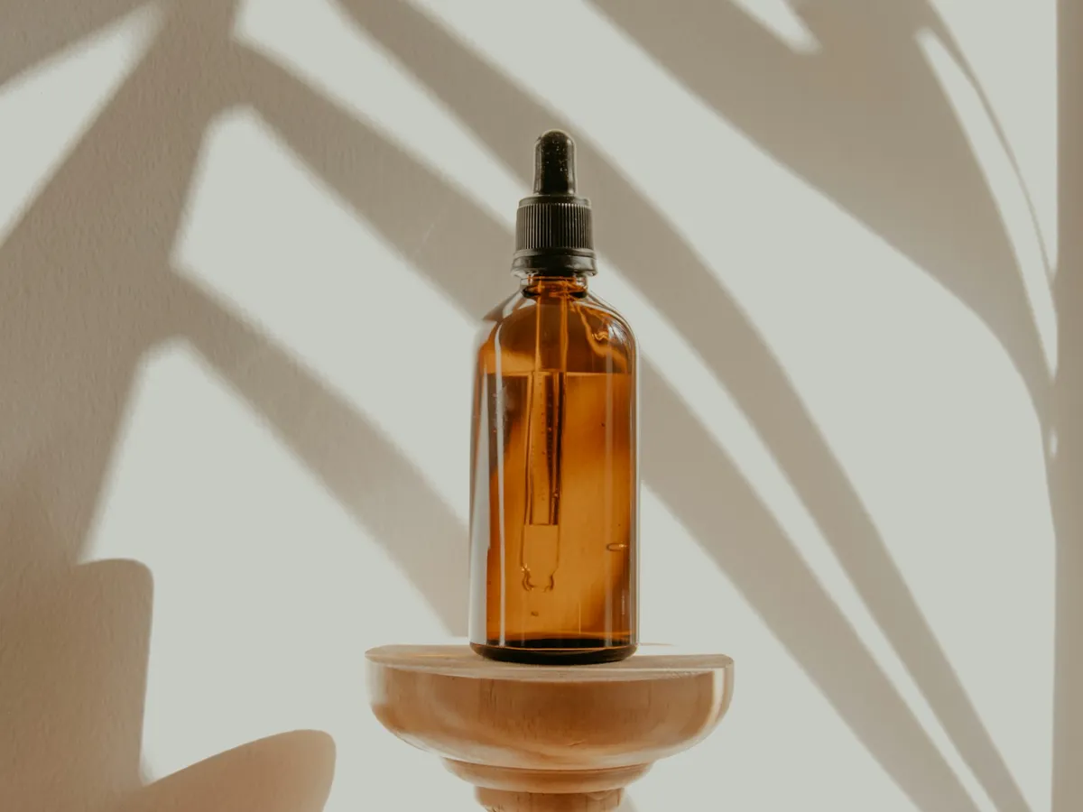 Amber dropper bottle on a wooden pedestal with palm-leaf shadows